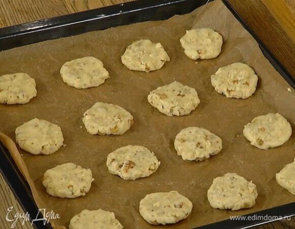Слепить из теста небольшие лепешки и выложить на противень, выстеленный бумагой для выпечки.