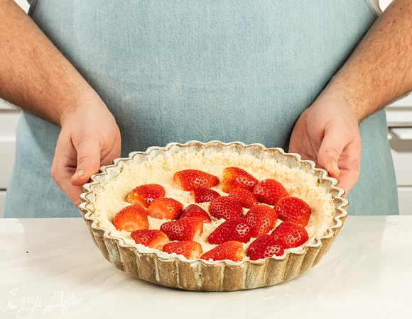 Форму для выпечки застелите пергаментом. Достаньте из холодильника тесто-крошку. На дно формы выложите половину теста. Далее выложите клубнику.