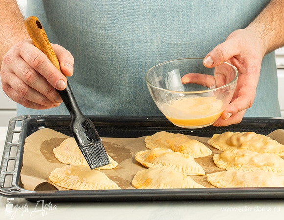 Противень застелите бумагой для выпечки, выложите пирожки. Яичный желток смешайте с 1 ст. л. молока и смажьте этой смесью заготовки.