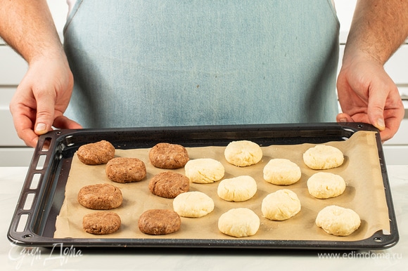 Сформируйте две «‎колбаски». Разделите каждую на небольшие кусочки и скатайте их в шарики. Выложите заготовки на застеленный противень, слегка прижмите и выпекайте при 180°С в течение 12 минут. Пока печенье остывает, растопите белый и темный шоколад.