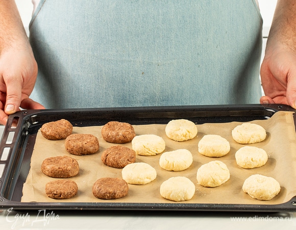 Сформируйте две «‎колбаски». Разделите каждую на небольшие кусочки и скатайте их в шарики. Выложите заготовки на застеленный противень, слегка прижмите и выпекайте при 180°С в течение 12 минут. Пока печенье остывает, растопите белый и темный шоколад.