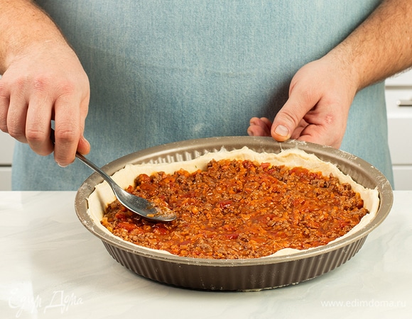 Посыпьте рабочую поверхность мукой и раскатайте вторую часть теста в пласт толщиной 3 мм, переложите в форму для запекания, выложите начинку из фарша, при необходимости обрежьте края.