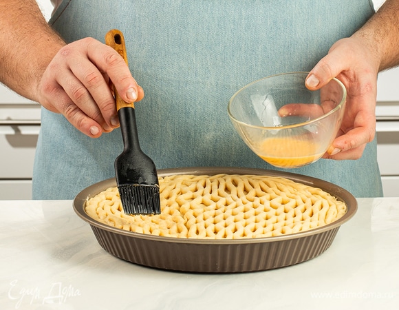 Аккуратно расправьте сетку и с помощью скалки переложите ее на верхушку пирога. Слой из яйца обеспечит хорошую сцепку деталей. Смажьте пирог оставшимся взбитым яйцом и отправьте в духовку, разогретую до 180°С.