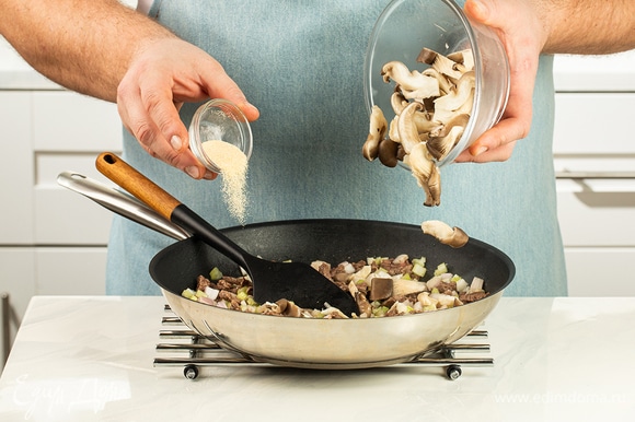 Выложите к мясу грибы, сельдерей и лук, добавьте сушеный чеснок.