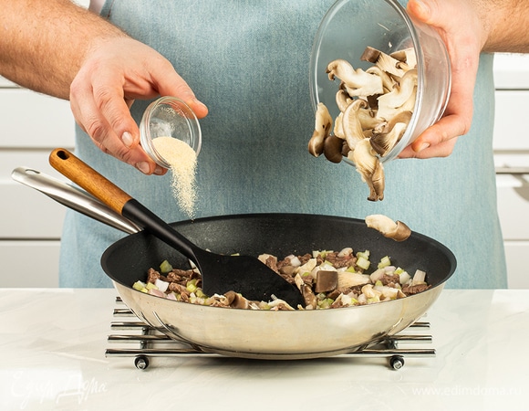 Выложите к мясу грибы, сельдерей и лук, добавьте сушеный чеснок.