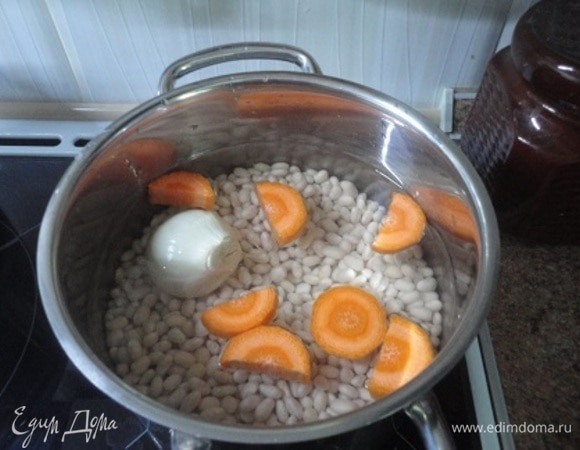Замочите фасоль на 8–10 часов. Залейте свежей водой в соотношении 1:5. Добавьте крупно нарезанную морковь и одну очищенную целую луковицу. Доведите до кипения, убавьте нагрев и варите 1,5 часа. Солить можно только в самом конце варки. Но обратите внимание, в этом рецепте мы будем добавлять чеснок, растертый с солью. За 5 минут до готовности добавьте лавровый лист.