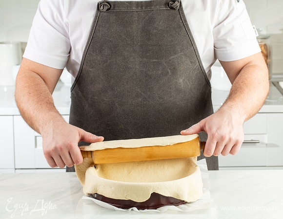 Снова посыпьте рабочую поверхность мукой. Раскатайте одну часть теста и переложите заготовку в форму с помощью скалки. Это основа пирога.