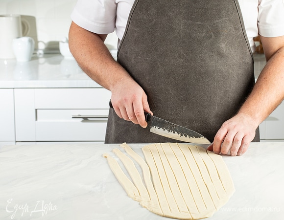 Опять припудрите рабочую поверхность мукой. Раскатайте вторую часть теста. Разрежьте его на ленты толщиной 1,5–2 см, не доходя до края.