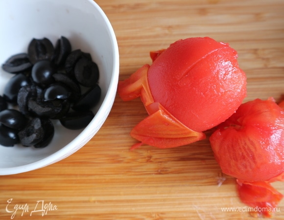 Приготовить помидоры. Нанести крестообразные насечки у плодоножки. На 30–40 секунд поместить в кипяток, снять шкурку, нарезать на кубики. Маслины нарезать на половинки.