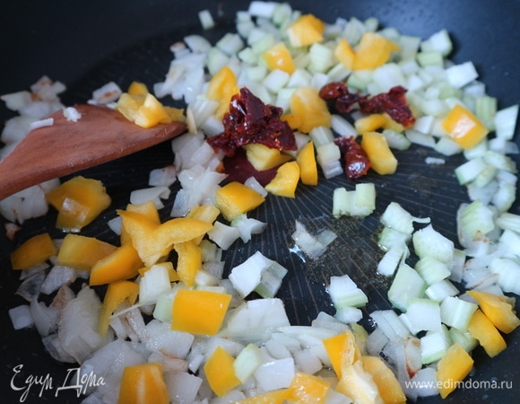 Разогреть сковороду с оливковым маслом и раздавленным с помощью ножа зубчиком чеснока, через некоторое время чеснок вынуть из сковороды, поместить лук, обжарить слегка (до прозрачности). Через несколько минут добавить сельдерей, болгарский перец, вяленые помидоры.