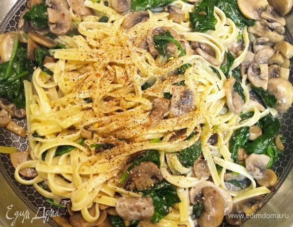 Тем временем паста сварилась, добавляем ее в сковороду с грибами, перемешиваем и готовим 1 минуту. Добавляем промытый шпинат, перемешиваем. Добавляем сливки. Возможно, понадобится добавить 2–3 ложки воды, в которой варилась паста. Я всегда отливаю полстакана этой воды, перед тем как сливать пасту. Это по рецепту. Если есть желание, вместо воды можете добавить больше сливок. Тогда получится более по-русски. Но менее по-итальянски. Все перемешиваем, добавляем свежемолотый перец. Пробуем на соль, при необходимости досаливаем. Прогреваем все вместе 2 минуты. Добавляем немного тертого пармезана. Перемешиваем.