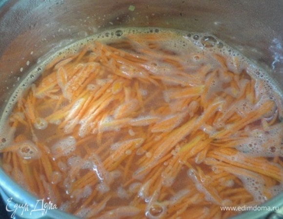 Морковь натрите на терке. В кастрюле с толстым дном разогрейте растительное масло и обжарьте в нем морковь. Добавьте рубленый чеснок, перемешайте и залейте горячим бульоном или водой.