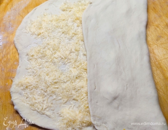 Тесто разделить на 2 части. Каждую часть раскатать в прямоугольник по размеру противня. Посыпать тертым сыром, сложить втрое. Нарезать полоски шириной 1 см. Перекрутить их и вытянуть в длину.