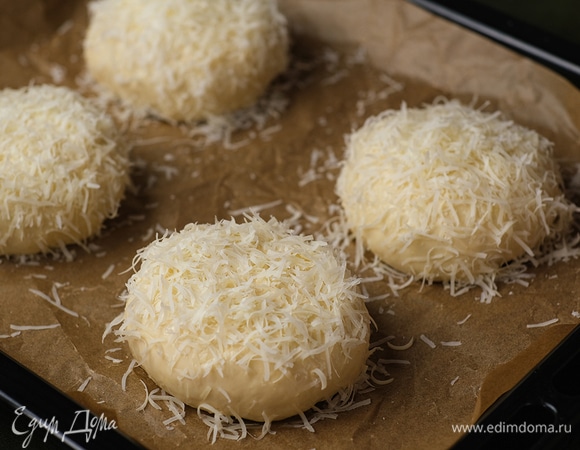 Противень застелите пергаментом и выложите на него булочки. Смажьте их яйцом и посыпьте пармезаном.