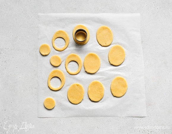 Тесто раскатайте в пласт толщиной 0,5 см. Вырежьте печенье в форме яйца. В половине заготовок сделайте круглые дырочки диаметром, равным диаметру персиков.