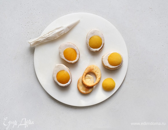 Смажьте все печенья глазурью и соберите: на целые заготовки выложите печенья с дырочкой, в центр поместите по половинке персика.