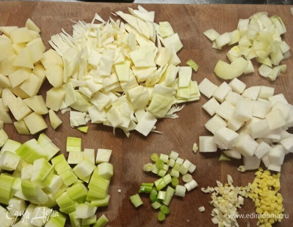 Сначала нужно подготовить все овощи. Очистить дайкон, кабачки, картофель, лук, чеснок и имбирь. С капусты удалить верхний лист. Все овощи промыть и обсушить. Капусту нашинковать квадратами. Картофель, дайкон и кабачок нарезать кубиками. Чтобы картофель не потемнел, его можно залить водой. Лук мелко нарезать. Чеснок и имбирь мелко нарубить. Нарезать белую часть зеленого лука.