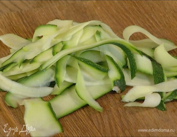 Цукини с помощью овощечистки нарезать тонкими полосками, затем разогреть в отдельной сковороде 2 ст. ложки оливкового масла и обжаривать цукини 1–2 минуты.