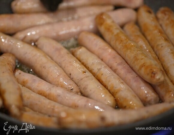 Бекон с луком и чесноком переложить в жаропрочную форму, а в сковороде обжарить колбаски до золотистого цвета и поместить на бекон с луком.
