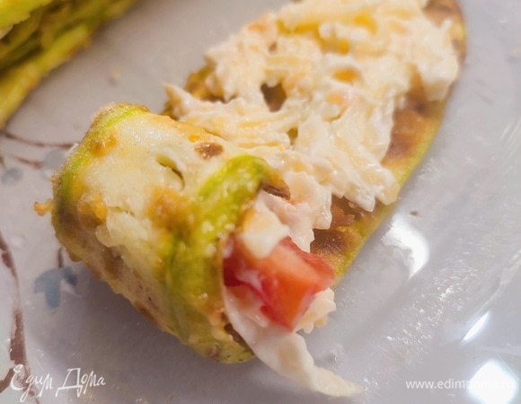 Сыр натереть на крупной терке. Смешать его с майонезом и чесноком, натертым на мелкой терке. Помидор нарезать на дольки. Кабачковые слайсы смазать сырной массой, положить дольку помидора и свернуть рулетом.