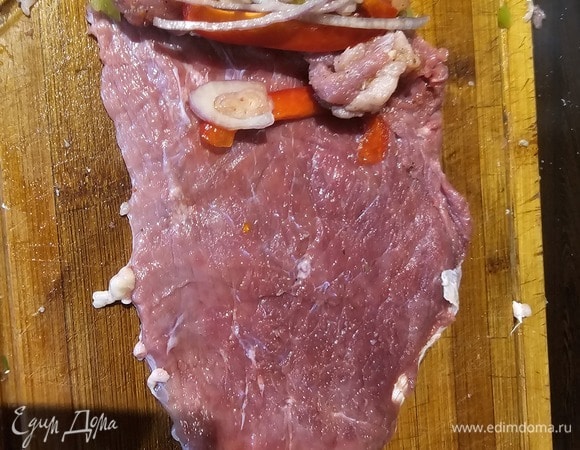 Внутрь нарезонного куска говядины положить небольшую колбаску из фарша, добавить перец и лук и свернуть рулетик.