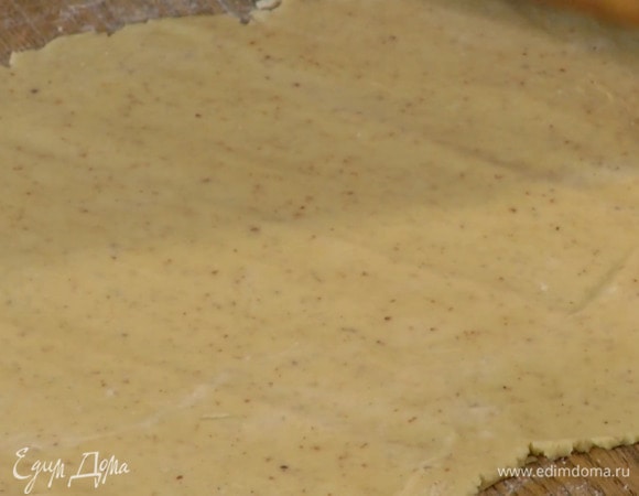 Рабочую поверхность присыпать оставшейся мукой и раскатать тесто не слишком тонко, затем выложить в выстеленную бумагой для выпечки разъемную форму и сформировать высокие бортики.