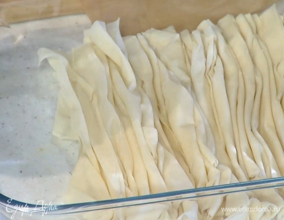 Тесто фило разрезать на небольшие прямоугольники и выложить по одному в стеклянную жаропрочную форму для выпечки, присобрав каждый гармошкой.