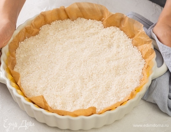 Выньте тесто из холодильника, положите на него пергамент и насыпьте рис. Выпекайте тесто с грузом 15 минут. Снимите пергамент и томите еще 10 минут.