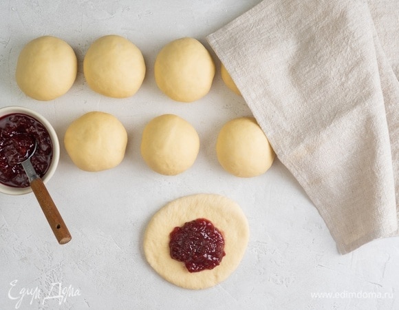 Аккуратно растяните каждую часть в лепешку. Выложите в центр ложку конфитюра и снова сделайте из теста шарики.