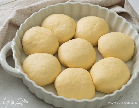 Уложите пышные булочки в форму диаметром 26–28 см, накройте сверху полотенцем и оставьте на 15–20 минут. За это время можно разогреть духовку до 180°C.