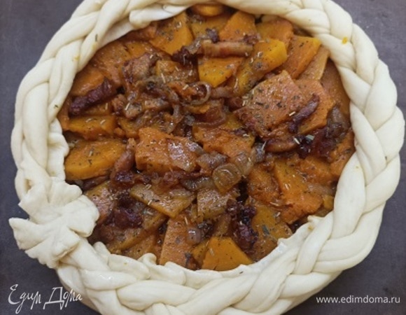 Раскатываем часть теста в круглый пласт толщиной 5–6 мм и перекладываем на противень. Выкладываем на тесто начинку ровным слоем, не доходя до края около 2 см. Формируем небольшие бортики.