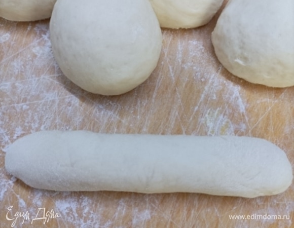 Подошедшее тесто обминаем и делим на 12 равных частей. Каждую часть округляем и даем полежать под полотенцем около 15 минут. Раскатываем каждую часть с помощью скалки в овальный пласт толщиной 3–4 мм и скручиваем в плотный длинный рулетик. Края тщательно защипываем. Должна получиться заготовка, напоминающая сосиску.