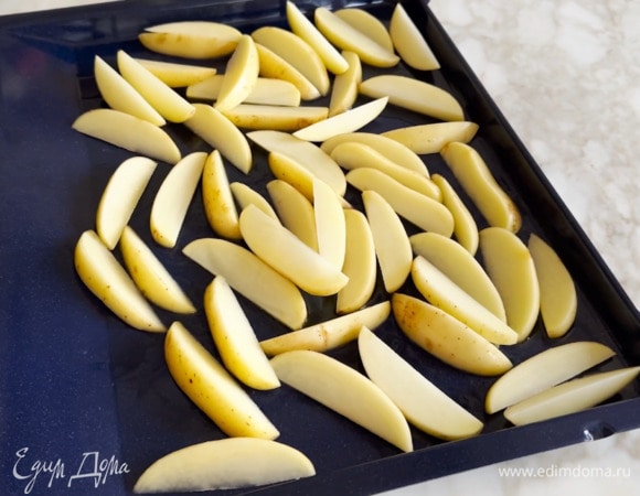 Картофель вымыть, просушить и, не очищая, нарезать дольками, затем выложить в один слой на смазанный оливковым маслом противень.