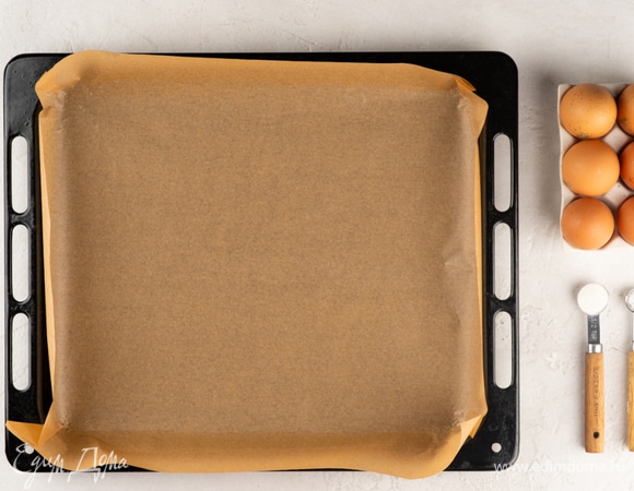 Застелите противень пергаментом, сделайте бортики. Разогрейте духовку до 170°C.