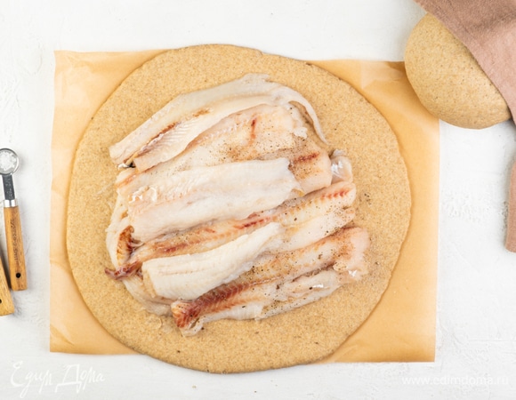 Поделите готовое тесто на две части. Раскатайте его на пласт толщиной в 1–2 см. На середину выложите рыбное филе, посолите и поперчите по вкусу. Закройте начинку второй частью теста.