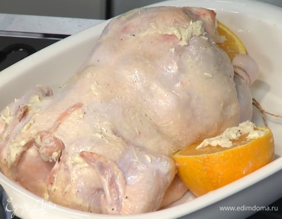 Второй апельсин разрезать пополам, выложить в форму рядом с курицей срезами вверх и смазать оставшимся сливочным маслом.