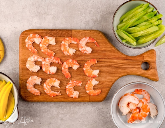 Очистите огурец от кожуры, нарежьте крупной соломкой. Манго очистите от кожицы и нарежьте дольками. Креветки разрежьте вдоль и пополам.