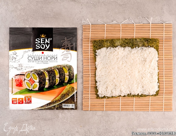 Положите на рабочую поверхность бамбуковый коврик и выложите на него лист нори Sen Soy. Сверху на него добавьте остывший рис и равномерно распределите его по всей поверхности, оставляя 2 см по верхнему краю.