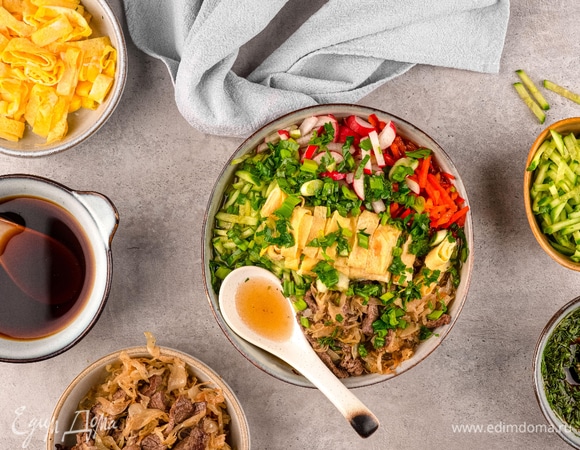 Разложите кукси в порционные чашки: на овощной салат положите лапшу, затем тушеную говядину с капустой и сверху нарезанный омлет, залейте блюдо заправкой с зеленью и предложите соус по вкусу.