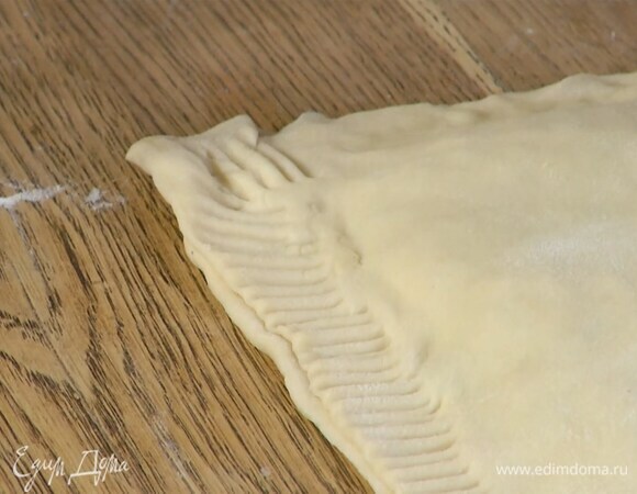 Размороженное тесто раскатать на присыпанной мукой рабочей поверхности в тонкий пласт и разрезать его пополам, на одну часть равномерно выложить начинку, отступая немного от краев, затем накрыть второй половиной теста и прижать края вилкой.