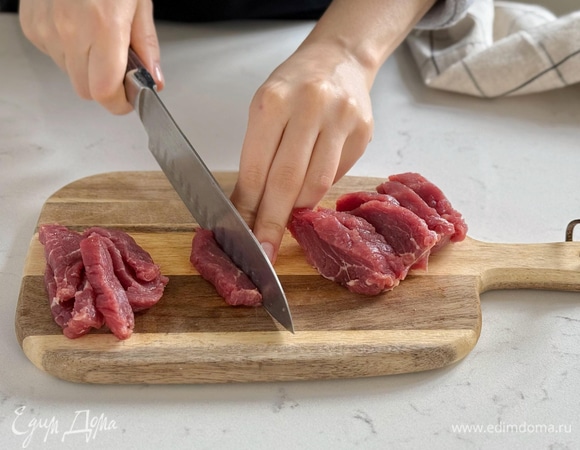 Удалите жилки и пленки с говядины. Нарежьте мясо ломтиками 0,5–1 см толщиной. Затем нарежьте его узкой соломкой.