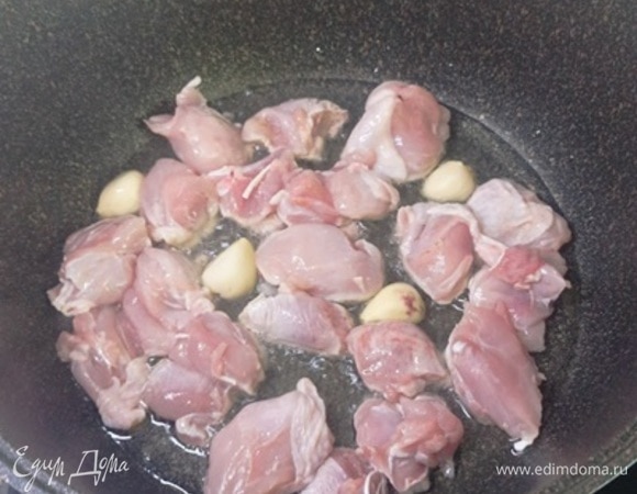Филе куриных бедер нарежьте кусочками. В сотейнике разогрейте оливковое масло. Положите филе и целые зубчики чеснока (можно даже не очищать). Готовьте на сильном огне 10 минут, помешивая, пока мясо не поджарится до румяной корочки.