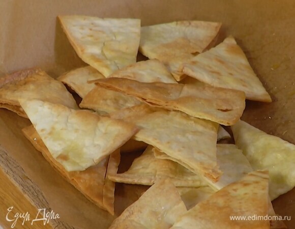 Питы нарезать треугольниками, выложить на выстеленный бумагой для выпечки противень, сбрызнуть оливковым маслом и запекать в разогретой духовке до золотистого цвета, затем слегка остудить и переложить в миску.