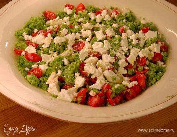 Кускус разрыхлить вилкой и выложить в большое блюдо, полить зеленой заправкой и частью оливкового масла, все посолить и перемешать. Добавить помидоры, еще раз перемешать, разложить сверху фету и полить оставшимся оливковым маслом.
