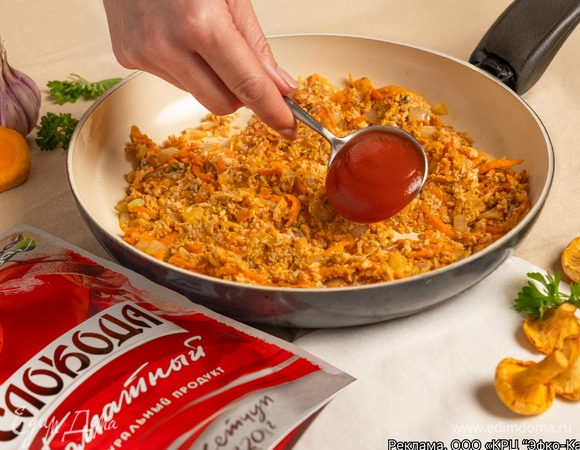 К пассерованным овощам добавьте шампиньоны и кетчуп «Слобода». Продолжайте жарить 15 минут, постоянно помешивая.