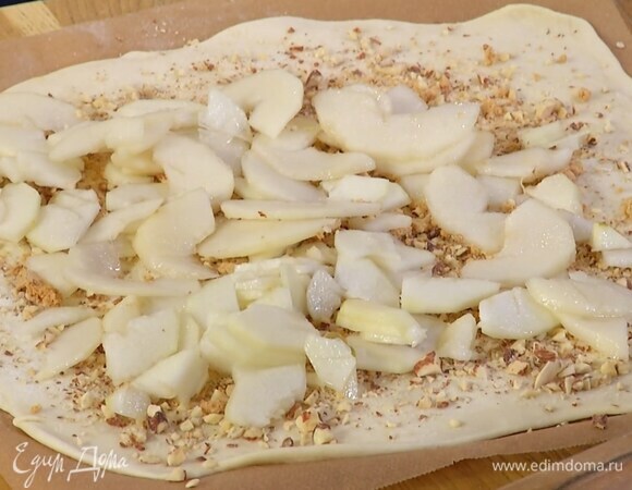 Посыпать раскатанное тесто миндалем, раскрошенным руками печеньем, сверху разложить дольки груш.