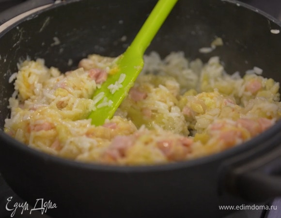 Готовый рис выложить в сотейник к овощам, все перемешать и выключить огонь, затем добавить ветчину, половину сыра, яйца и зелень, все посолить и перемешать.