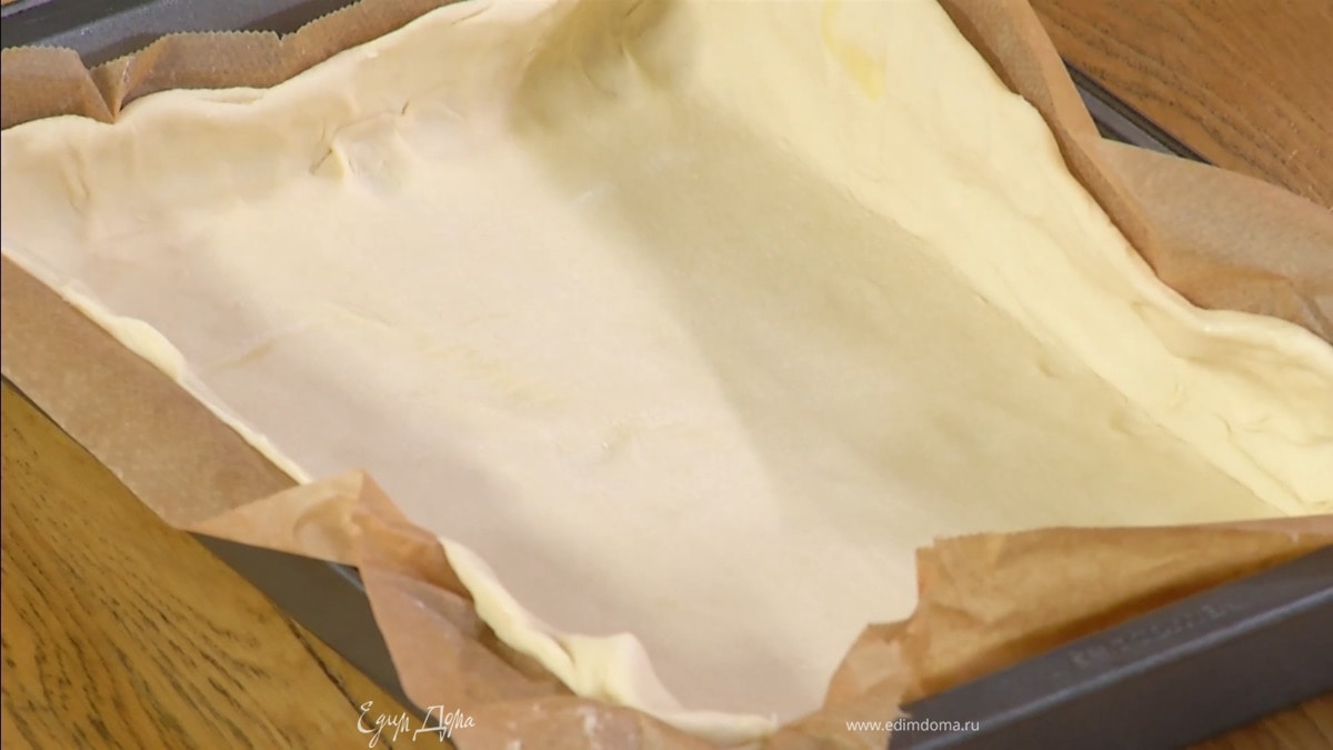 Тесто предварительно разморозить, затем раскатать на бумаге для выпечки в тонкий пласт и вместе с бумагой выложить в небольшую форму.