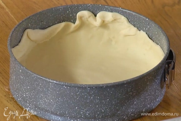 Разрезать размороженное тесто на две неравные части. Большую часть тонко раскатать, выложить в выстеленную бумагой для выпечки разъемную форму, сформировав бортики.