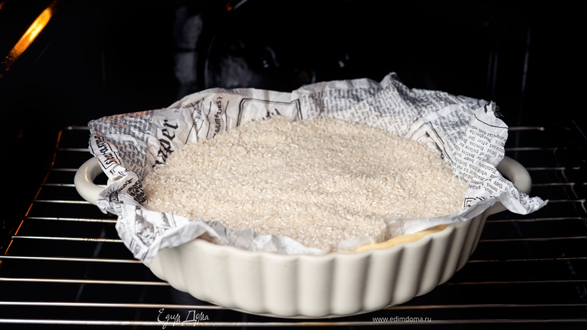 Накройте тесто пергаментной бумагой и положите на него груз. Выпекайте в разогретой духовке при 180°C 20 минут.